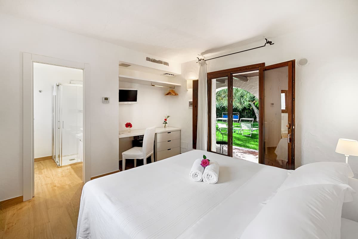 A hotel room with a bed, a desk, a chair, and a view of a garden.