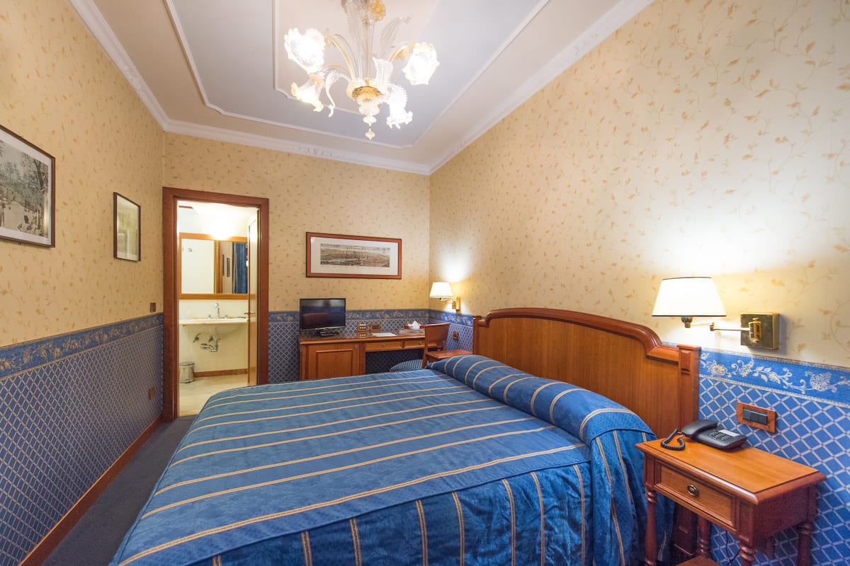 Une chambre d’hôtel avec un grand lit, un bureau avec un ordinateur, un téléphone et une table de chevet.