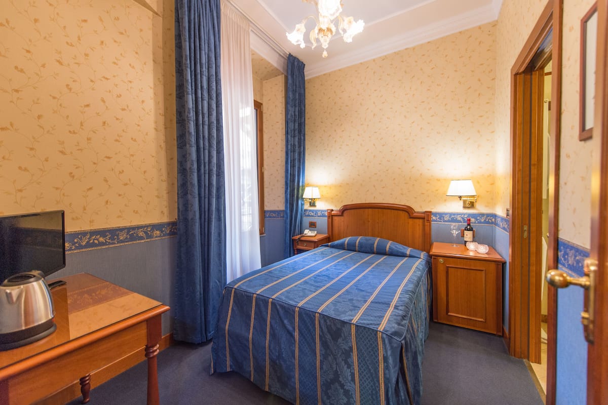Une chambre d’hôtel comprenant un lit, un bureau avec une bouilloire, une télévision et deux lampes de chevet.