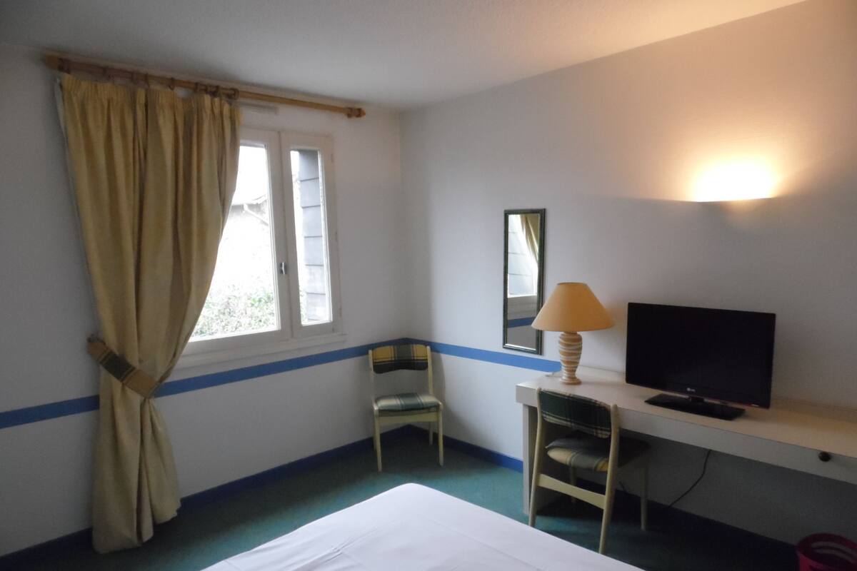 Een hotelkamer met een bed, een bureau met een lamp, een stoel, een televisie en een raam met gordijnen.