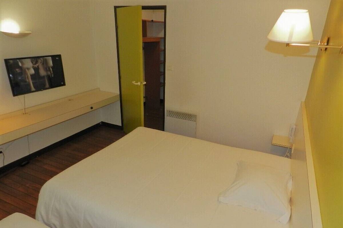 Een slaapkamer met twee bedden, een televisie op een standaard, en een deur die naar een andere kamer leidt.