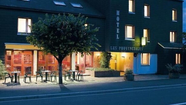 A hotel with a dark facade, multiple windows, and outdoor seating. - Hotel Les Provinciales (Arpajon-sur-Cere)