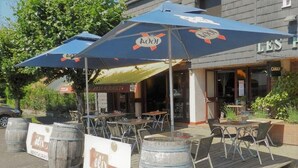 An outdoor café with wooden tables and chairs, a blue umbrella, and a sign for 'élix café'. - Hotel Les Provinciales (Arpajon-sur-Cere)