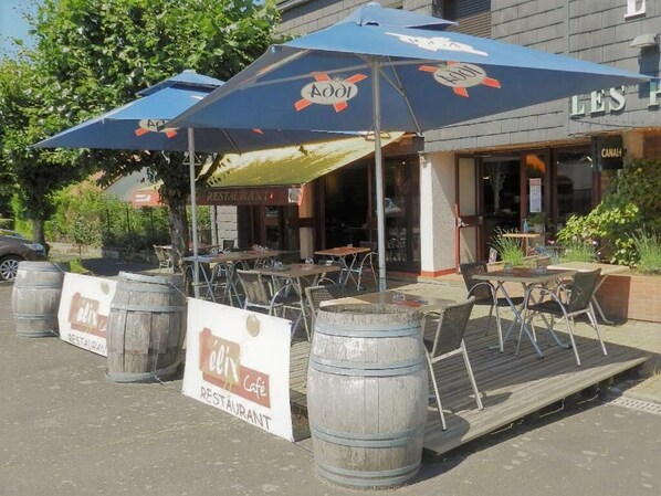 Un café al aire libre con mesas y sillas de madera, una sombrilla azul y un letrero que dice 'élix café'.