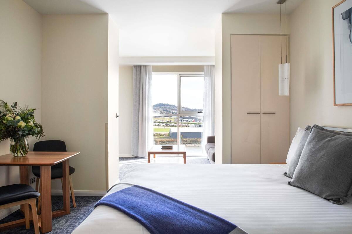 A hotel room with a bed, a desk with a chair, a window with a view, and a wardrobe.