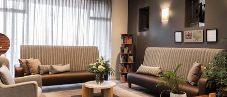 A modern living room with a sofa, armchair, coffee table, bookshelf, and a potted plant.