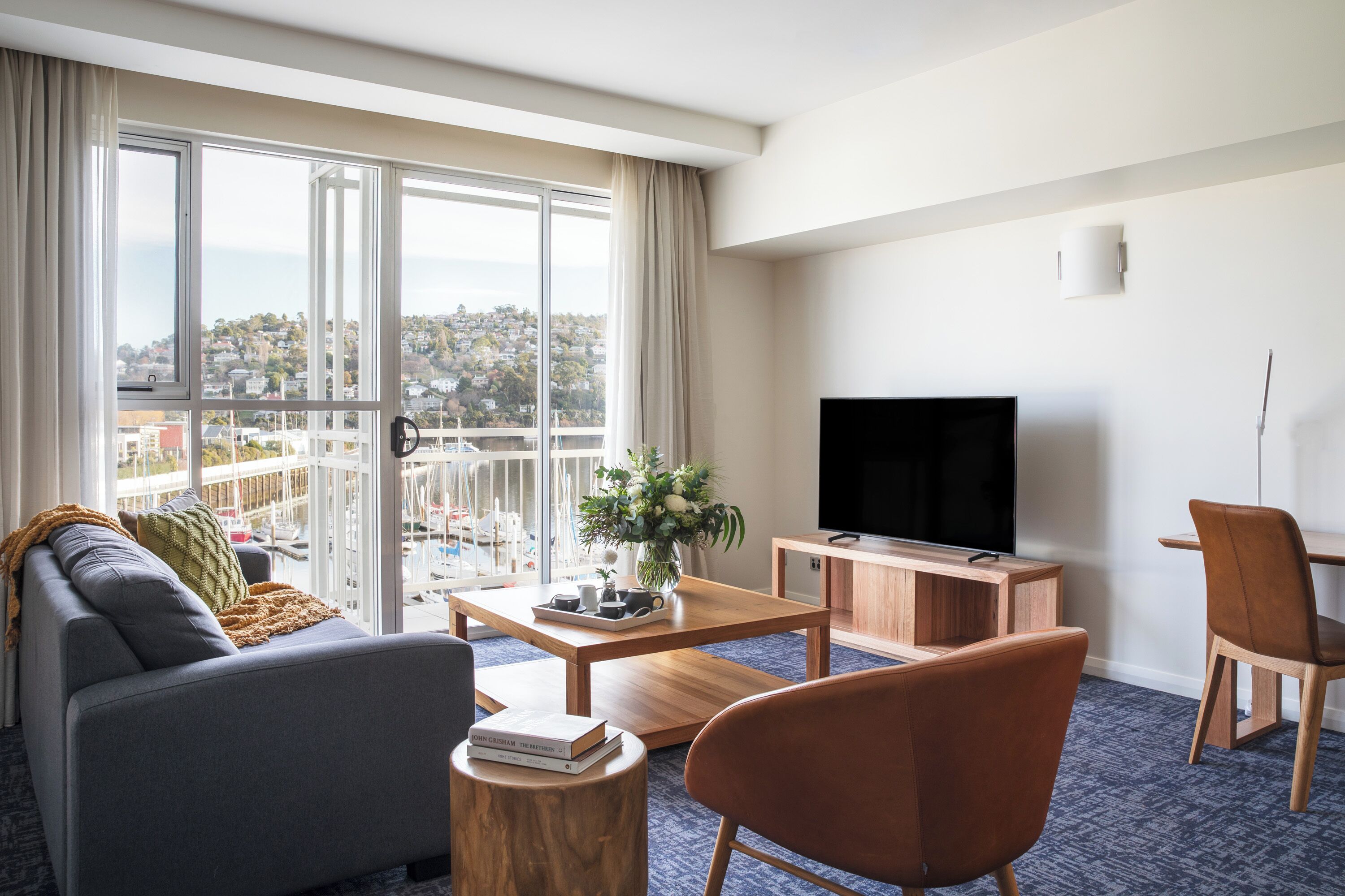 Una habitación de hotel moderna con un ventanal grande, un sofá, una mesa de centro, un televisor y un armario de madera.