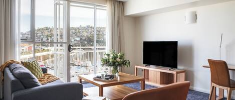 Una habitación de hotel moderna con un ventanal grande, un sofá, una mesa de centro, un televisor y un armario de madera.