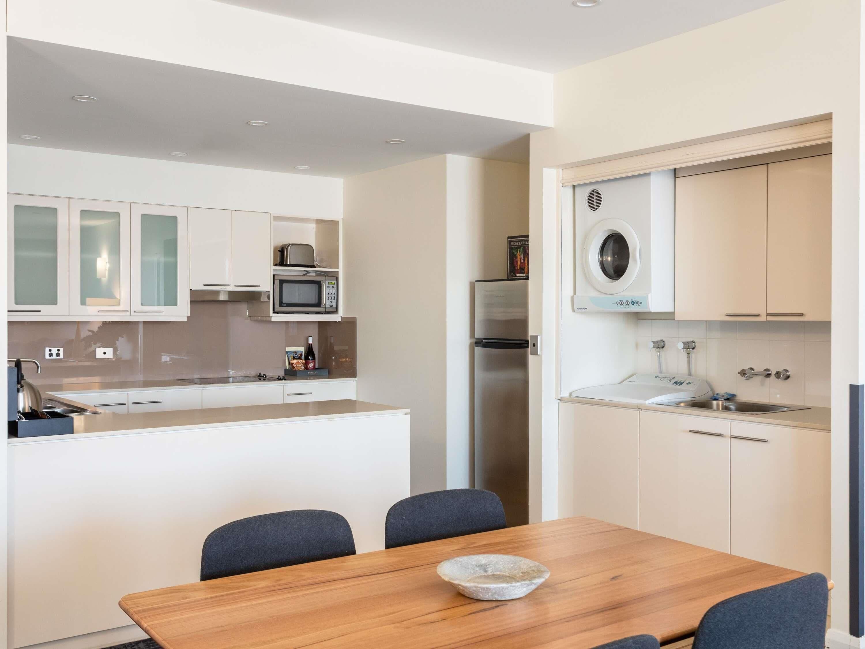 A modern kitchen with white cabinets, a microwave, a refrigerator, and a washing machine.