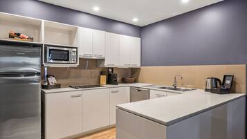 Una cocina moderna con gabinetes blancos, un refrigerador de acero inoxidable, un microondas y una cafetera.