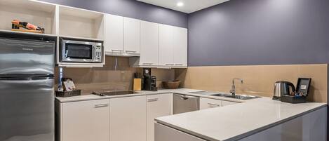 A modern kitchen with white cabinets, a stainless steel refrigerator, a microwave, and a coffee maker.