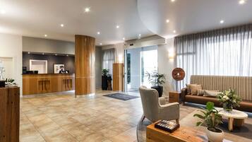 A modern hotel lobby with a reception desk, seating area, and a large window with curtains.