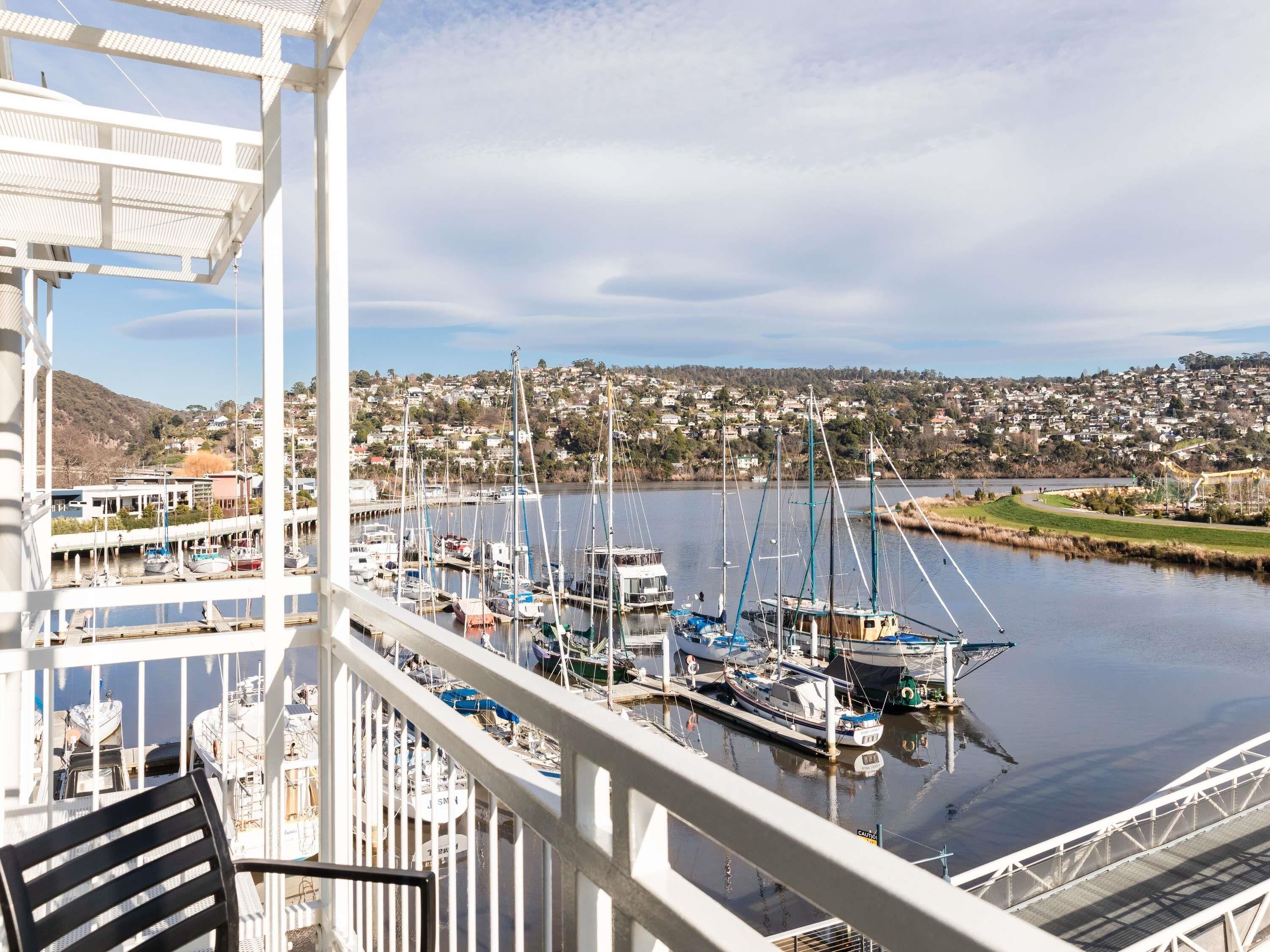 A marina with boats docked, a view of a residential area, and a balcony with a chair.