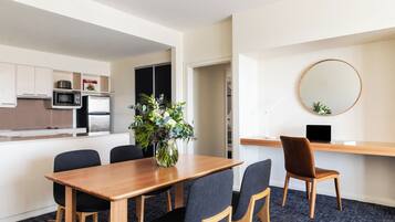 Una cocina moderna con microondas, estufa y armarios. Hay una zona de comedor con mesa y sillas de madera, y un escritorio pequeño con una computadora portátil y un jarrón de flores.