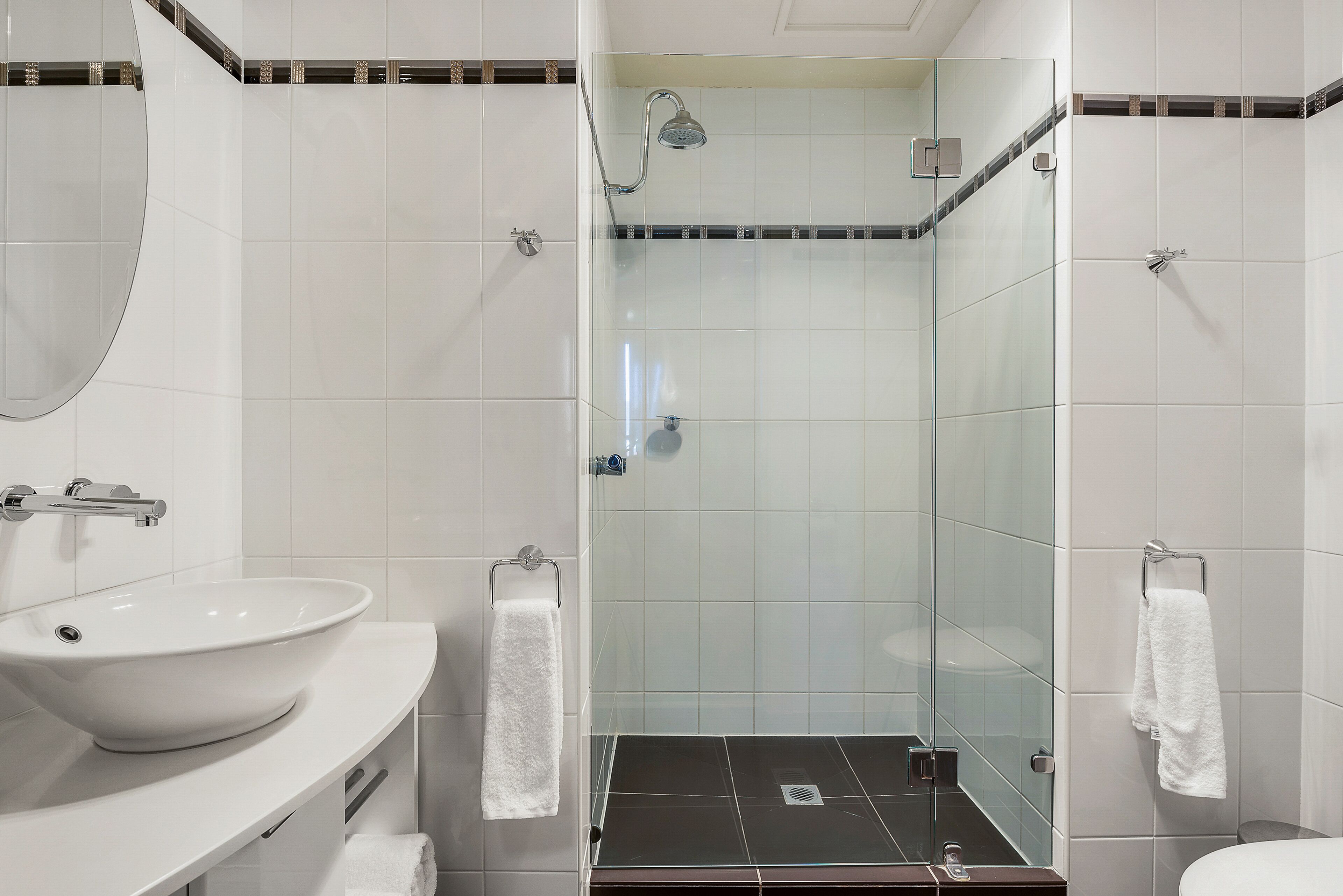 A modern bathroom with a large white sink, a glass shower enclosure, and a mirror.