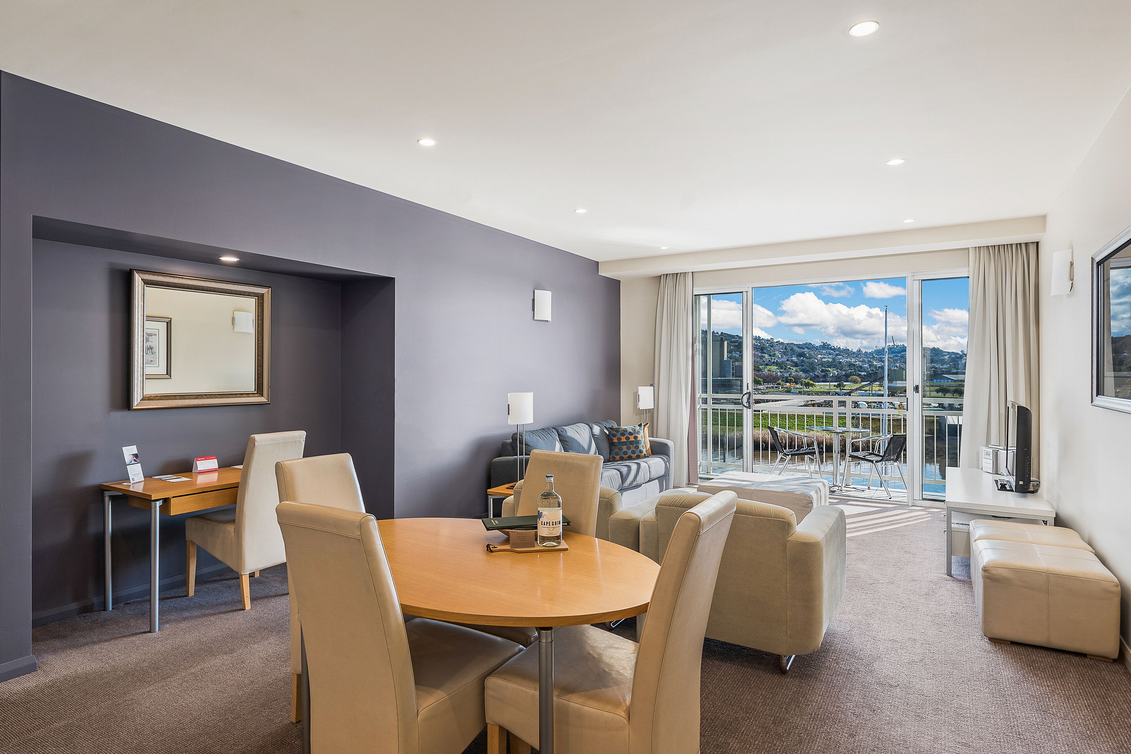 A hotel room with a dining area, a sofa, and a balcony with a city view.