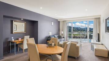 A hotel room with a dining area, a sofa, and a balcony with a city view.