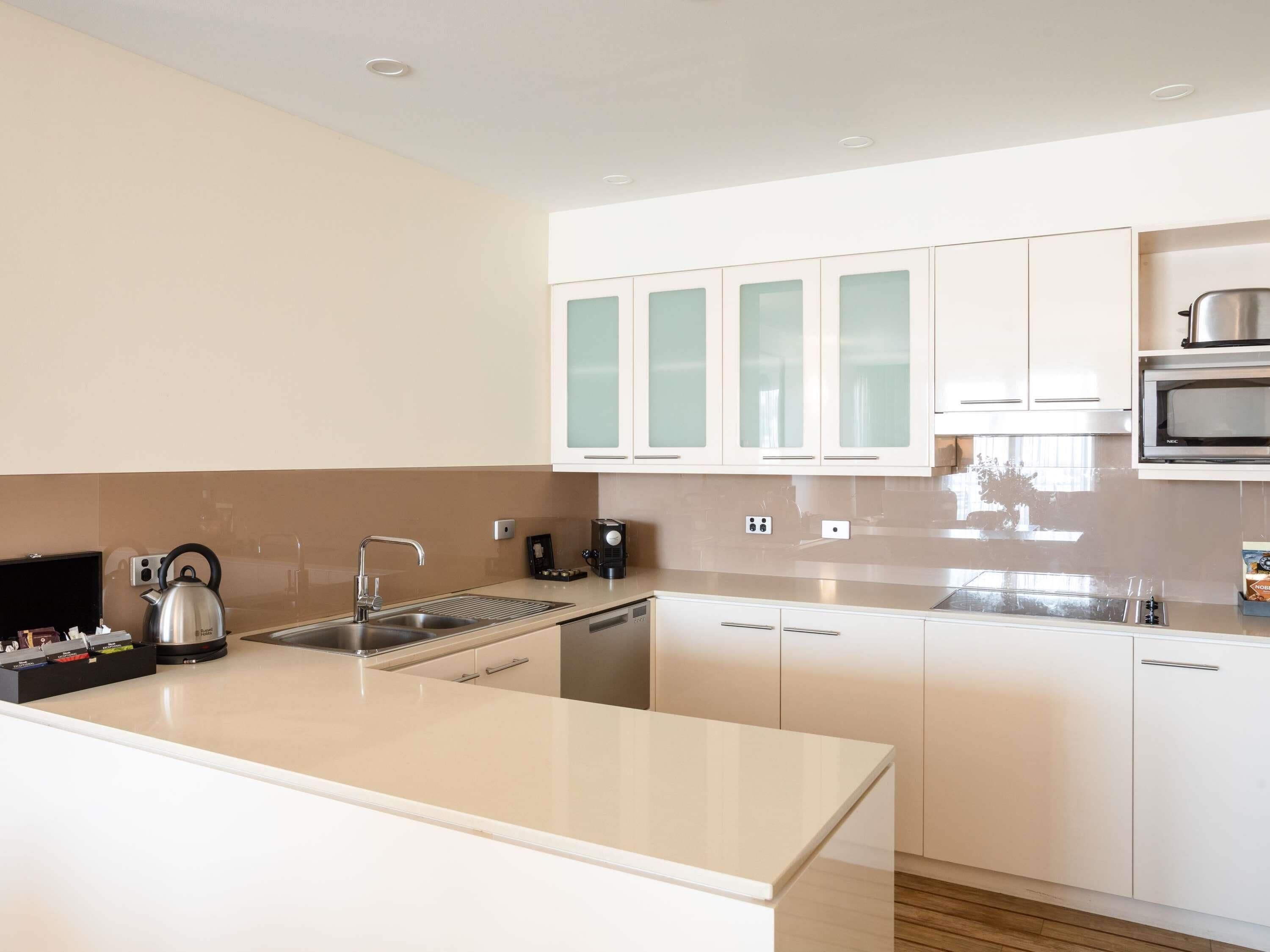 A modern kitchen with white cabinets, a stainless steel kettle, a microwave, and a coffee maker.