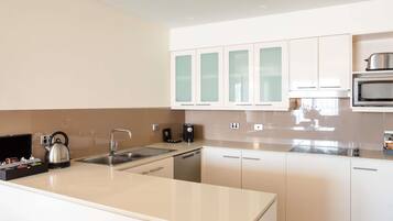 A modern kitchen with white cabinets, a stainless steel kettle, a microwave, and a coffee maker.