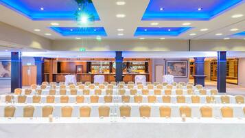 Un salón de conferencias con filas de mesas y sillas, una zona de bar e iluminación azul en el techo.