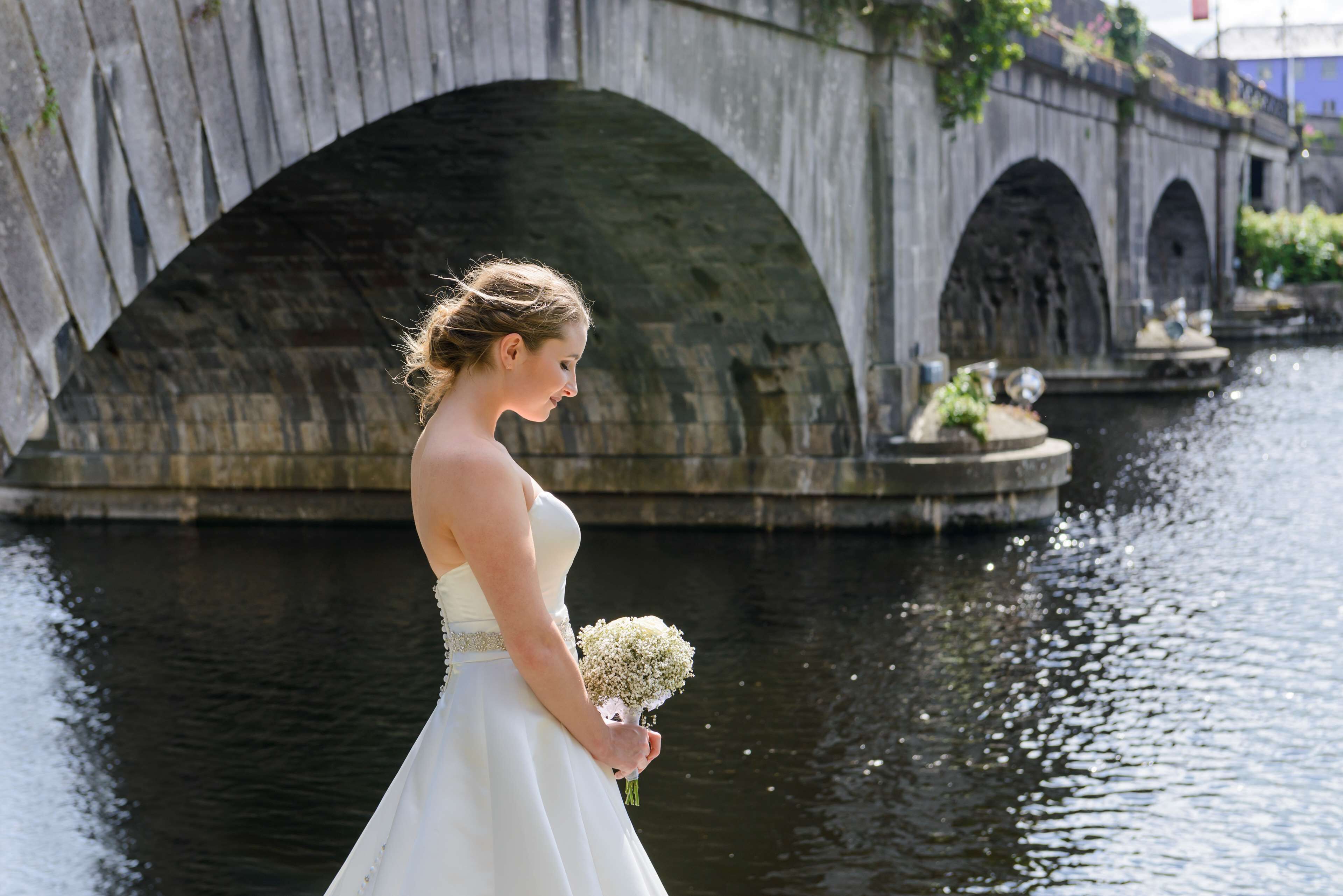 Una persona con un vestido blanco parada junto a un canal con puentes de piedra al fondo.