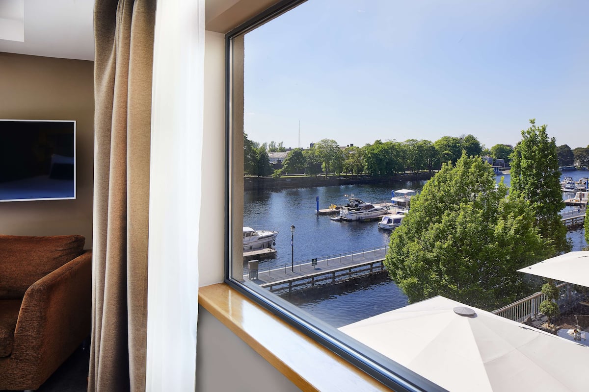 Habitación con ventana grande que da a un puerto deportivo con barcos y un árbol.