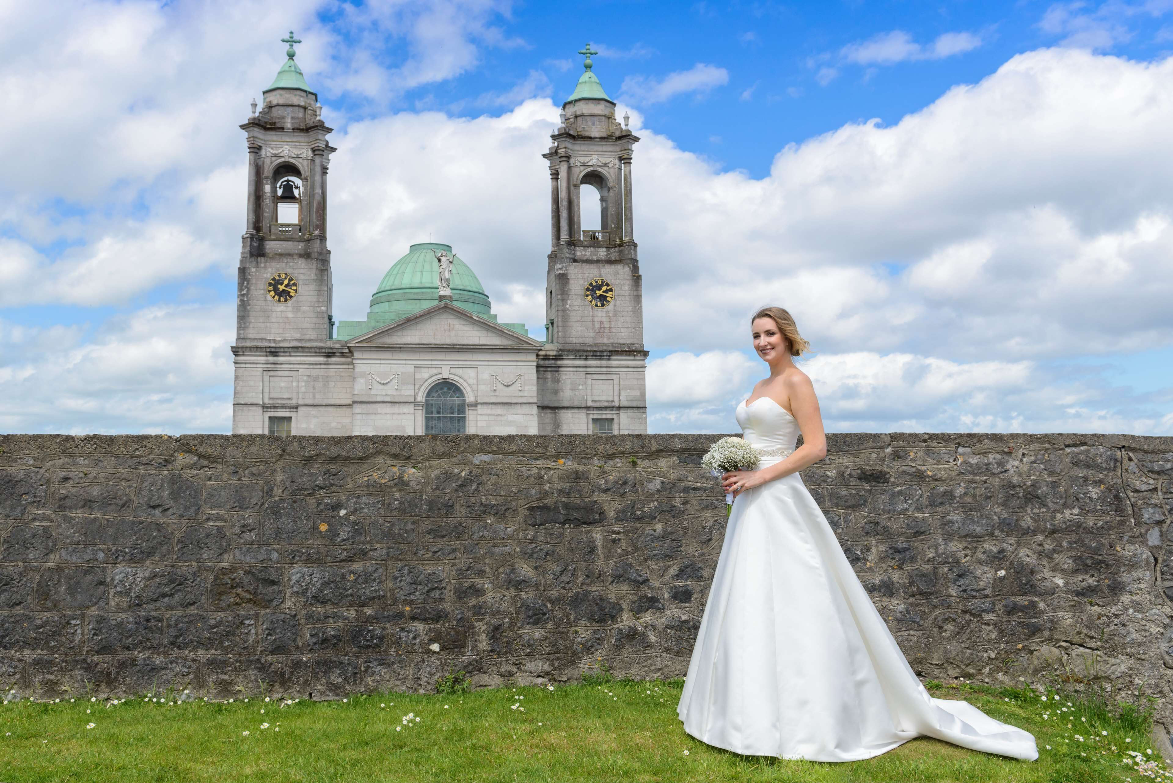 A bride in a white dress standing in front of a historic church with two bell towers and a green dome.