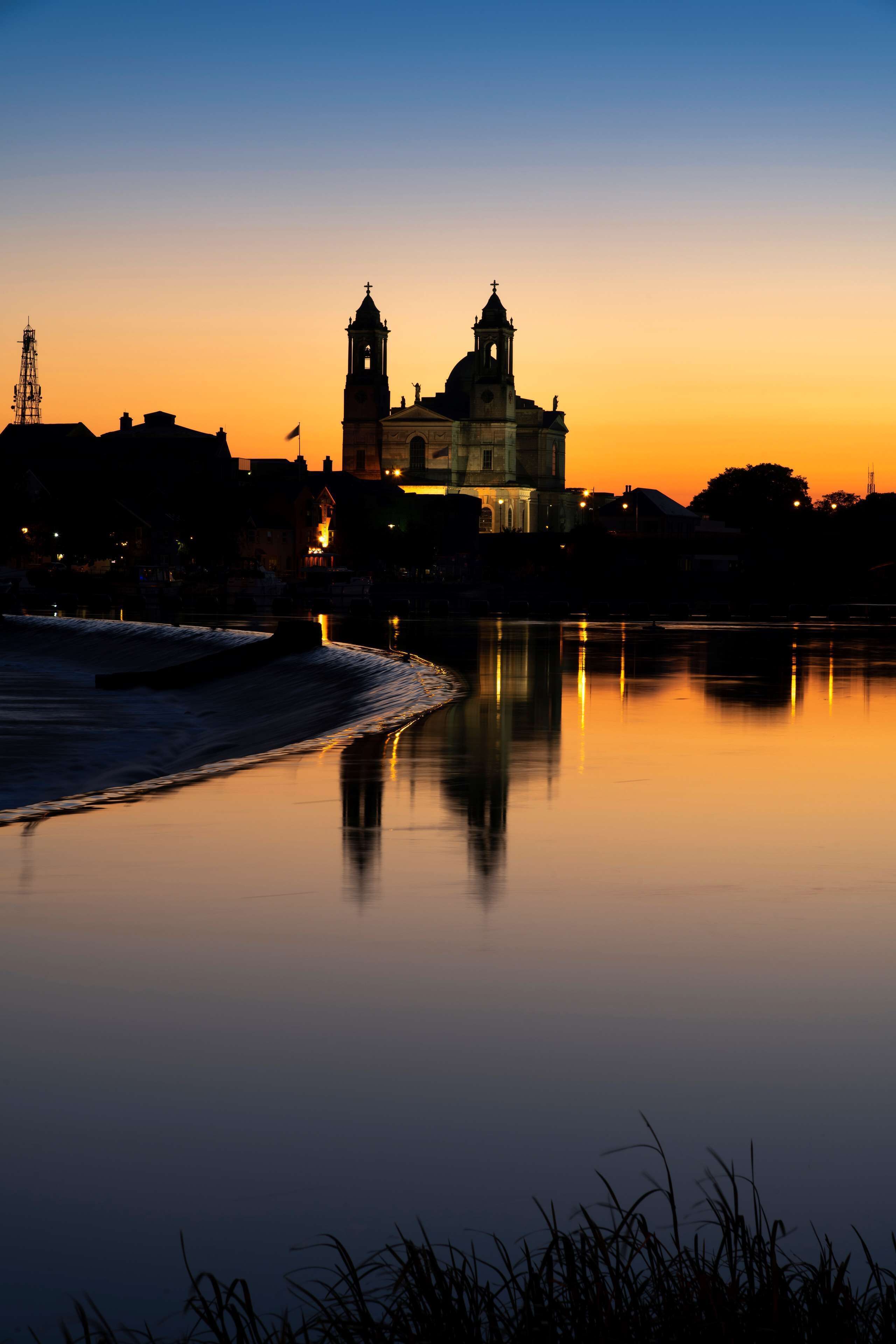 Una orilla tranquila de agua con una iglesia destacada y una torre que se refleja en el agua.