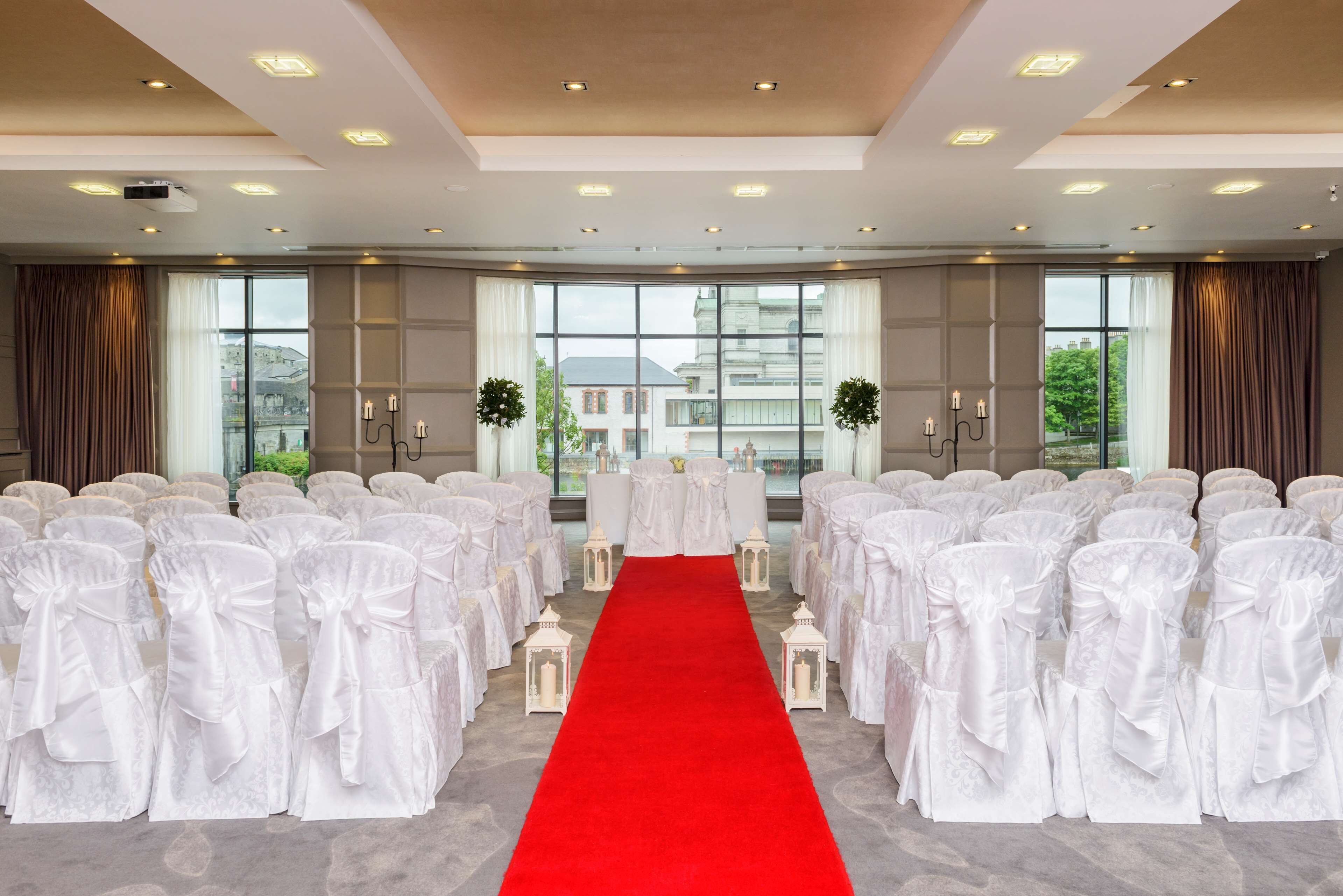 A conference room with white chairs, a red carpet aisle, and large windows with curtains.