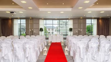 A conference room with white chairs, a red carpet aisle, and large windows with curtains.