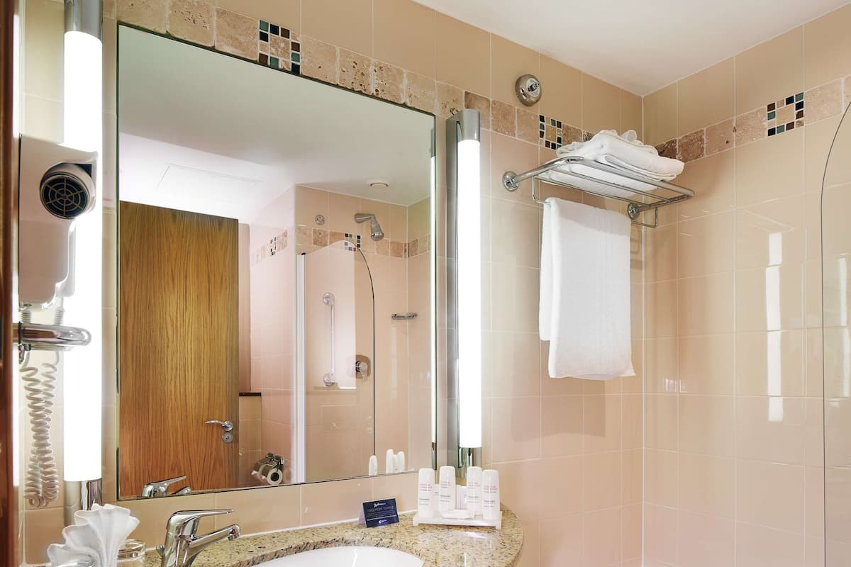 Un baño moderno con lavamanos de granito, un espejo grande, ducha con cerramiento de vidrio y tocador de madera oscura.