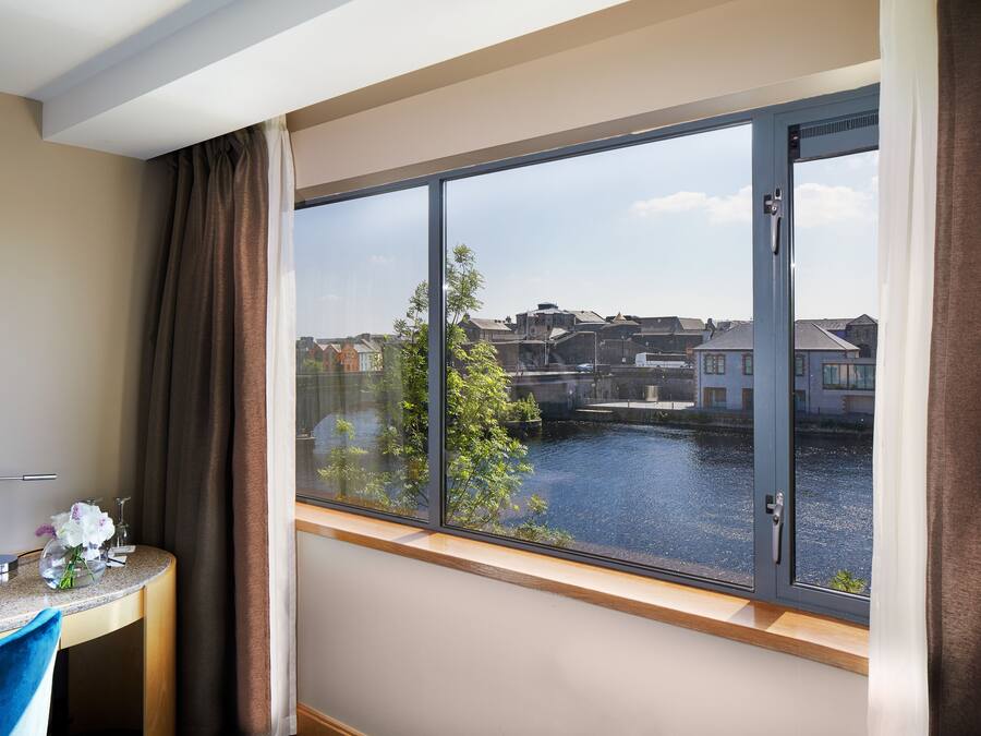 A hotel room with a large window offering a view of a canal and buildings.