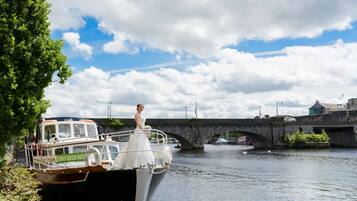 Une scène de mariage avec une mariée à bord d’un bateau amarré à un pont enjambant une rivière.