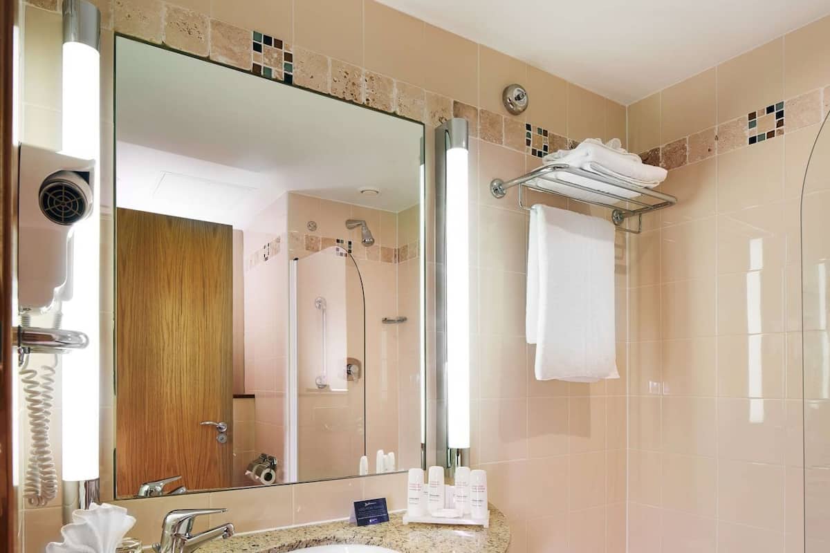 Un baño moderno con lavamanos de granito, un espejo grande, ducha con mampara de vidrio y tocador de madera oscura.