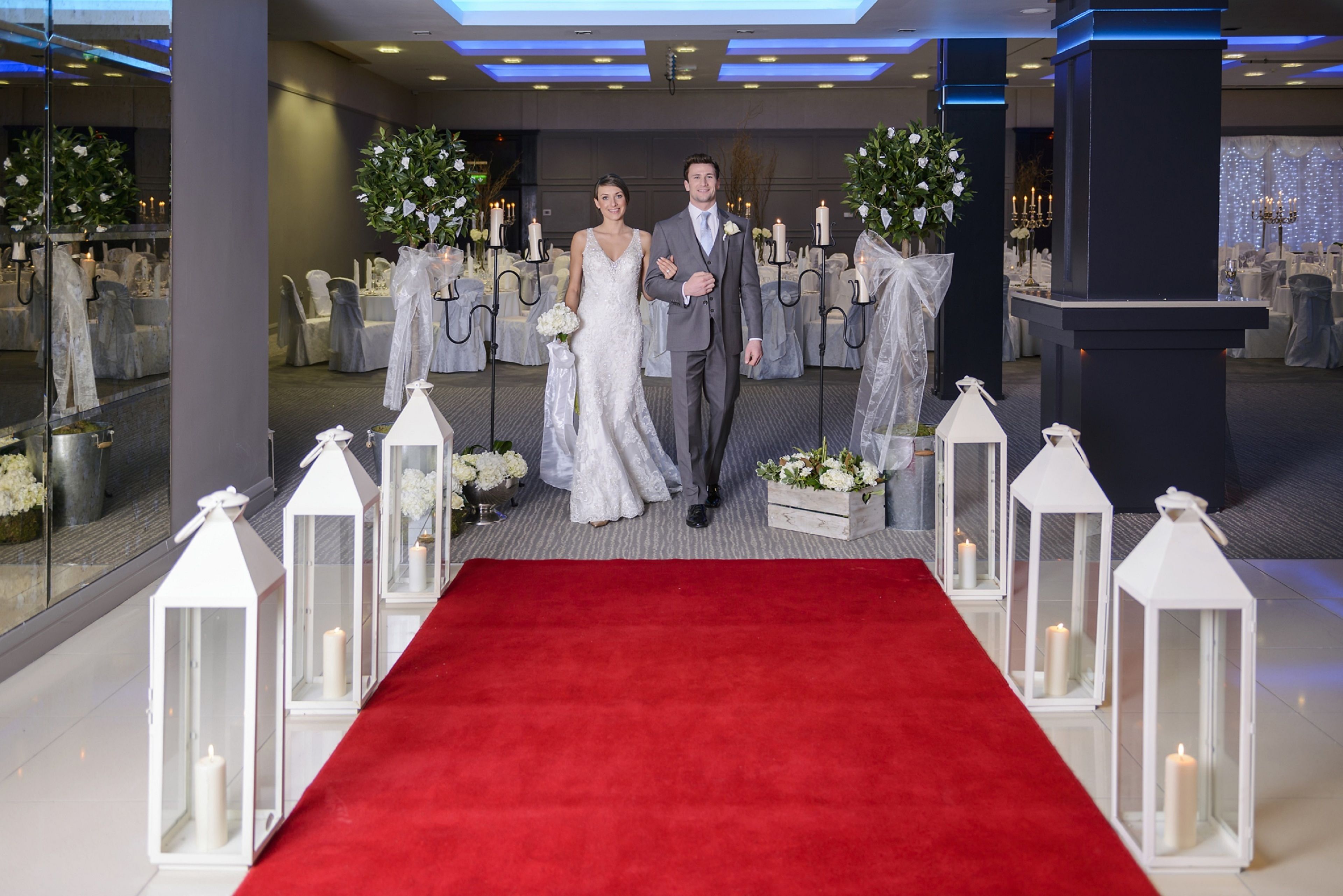 A red carpet aisle with white lanterns and floral arrangements.