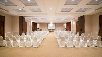 A conference room with rows of white-covered chairs, a projector screen, and a carpeted floor.