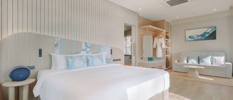 A modern hotel room with a large bed, bedside tables, a wardrobe, a seating area, and a painting on the wall.