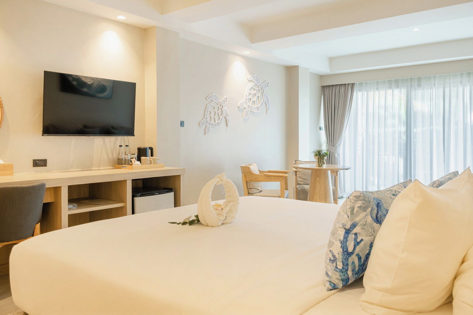 Quarto de hotel com uma cama grande, uma escrivaninha com televisão de tela plana, uma mesinha e uma cadeira.