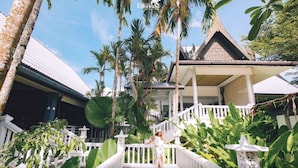 Un resort tropical con un porche cubierto, barandillas blancas y abundante vegetación.
