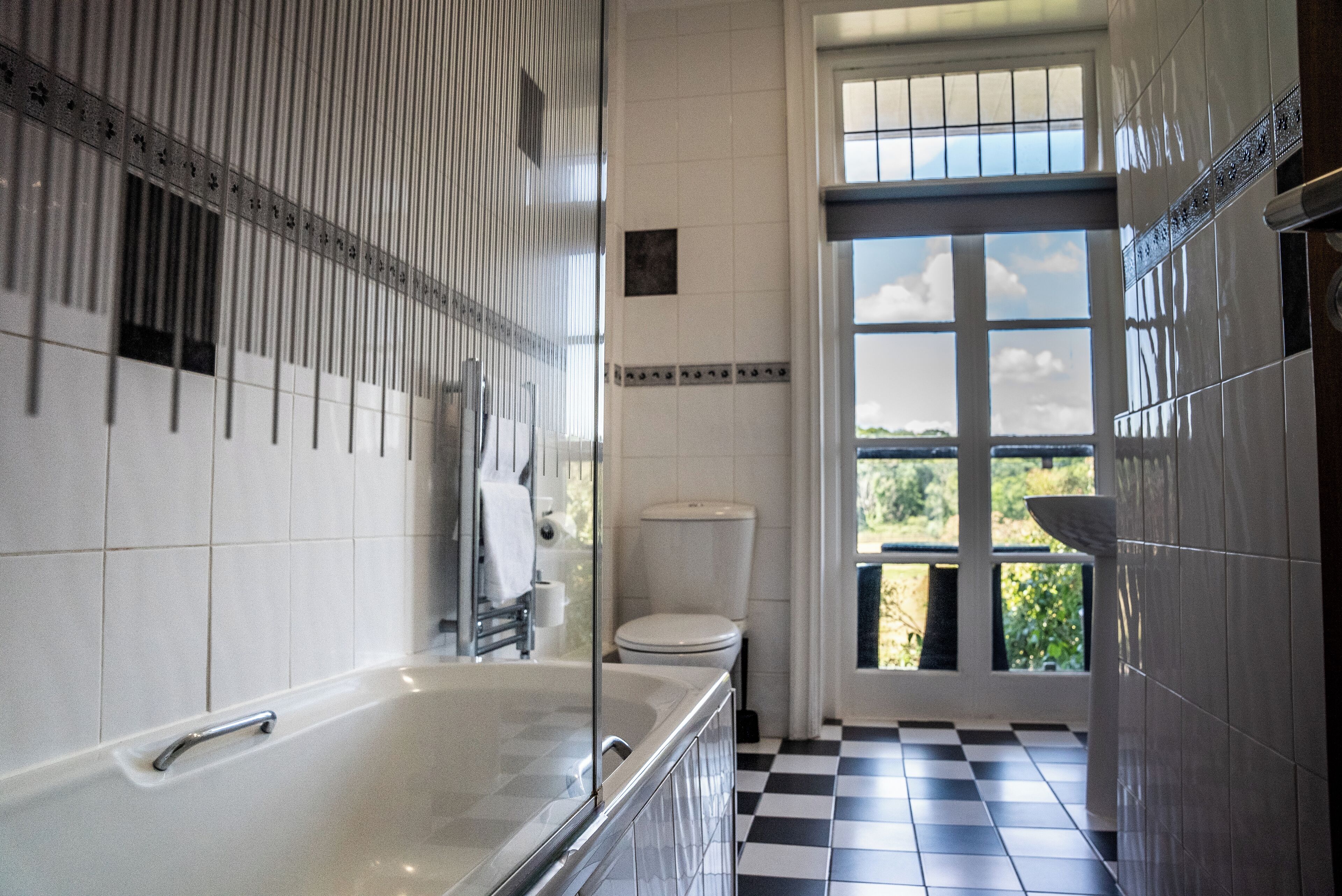 Un baño con bañera, inodoro y ventana con vistas a zonas verdes.