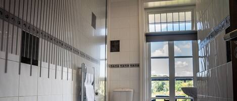 Un baño con bañera, inodoro y ventana con vistas a zonas verdes.