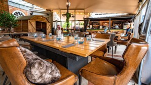 A restaurant with a large wooden table, leather chairs, and a bar area in the background. - Balmer Lawn Hotel (Brockenhurst)