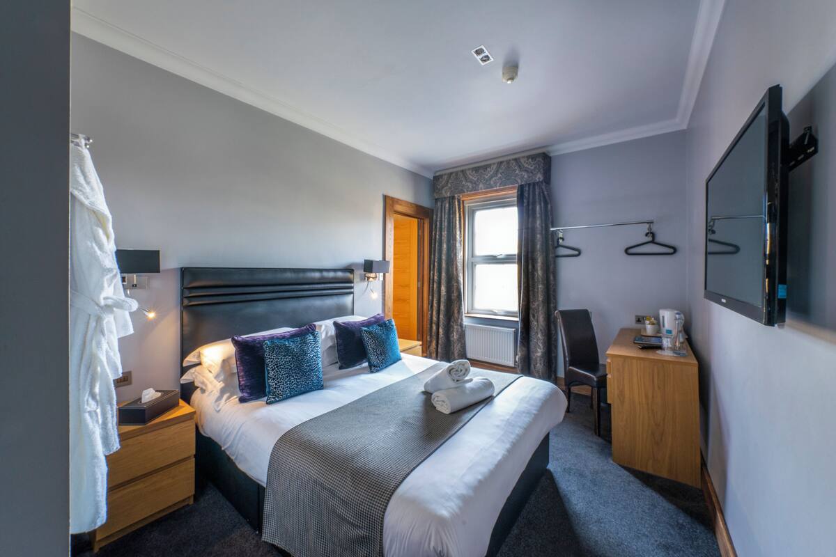 A hotel room with a bed, bedside table, and a TV mounted on the wall.