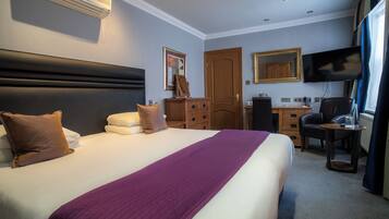 A hotel room with a large bed, a desk, a chair, a television, and a wardrobe.