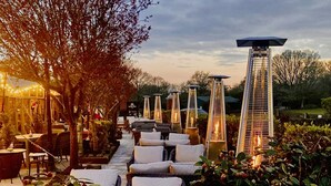 An outdoor seating area with white cushioned chairs and tables, surrounded by tall, narrow lantern-style lights. - Balmer Lawn Hotel (Brockenhurst)