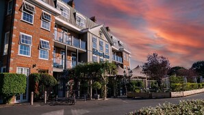 A multi-story building with a prominent 'Barber Lane' sign, featuring a mix of brick and modern architectural styles, surrounded by greenery and street lamps. - Balmer Lawn Hotel (Brockenhurst)
