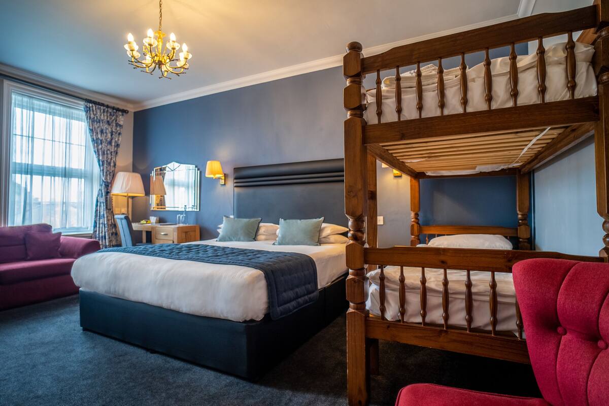 A bedroom with a bunk bed, a desk, a chair, a lamp, and a window with curtains.