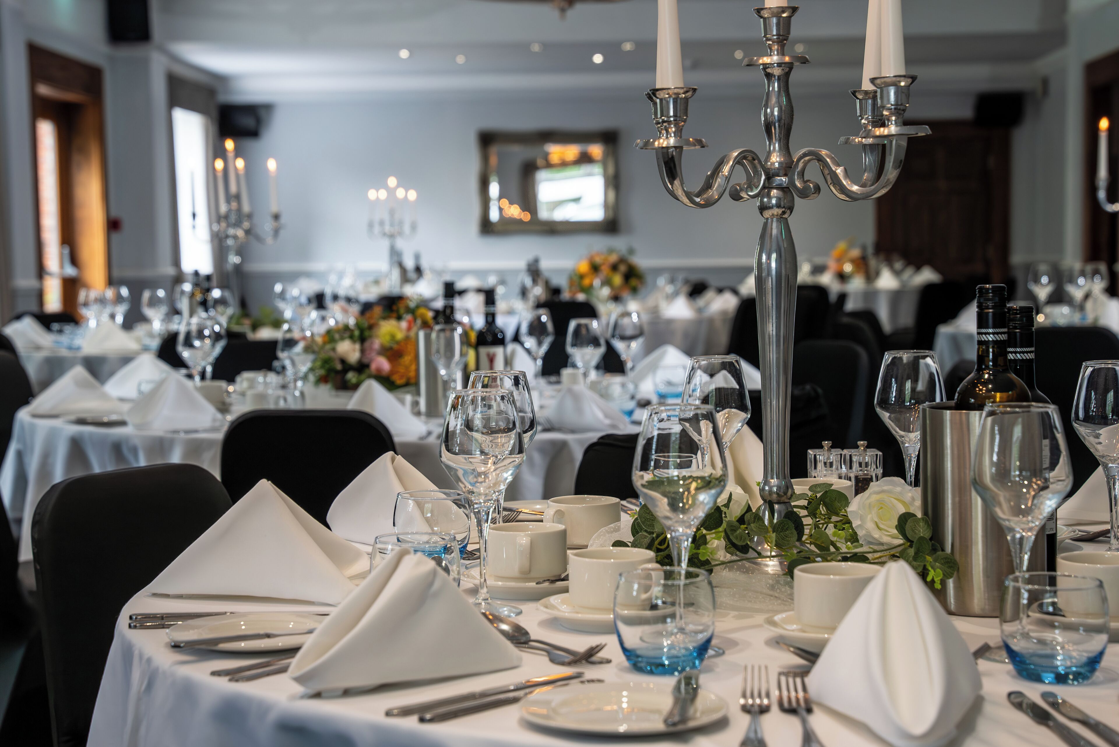 Una mesa de comedor elegantemente dispuesta, con manteles blancos, cubiertos y copas de vino, que sugiere una experiencia gastronómica formal.