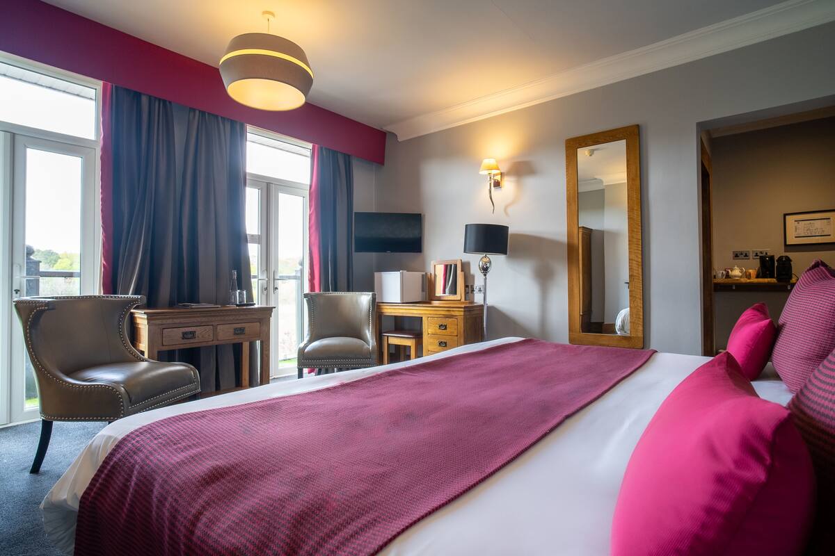 A hotel room with a large bed, a desk, a chair, a TV, and a mirror.
