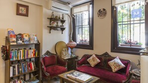A cozy room with a bookshelf, a red sofa, and a window with a view of greenery. - Naz Wooden House Inn - Byzantine House (Istanbul)